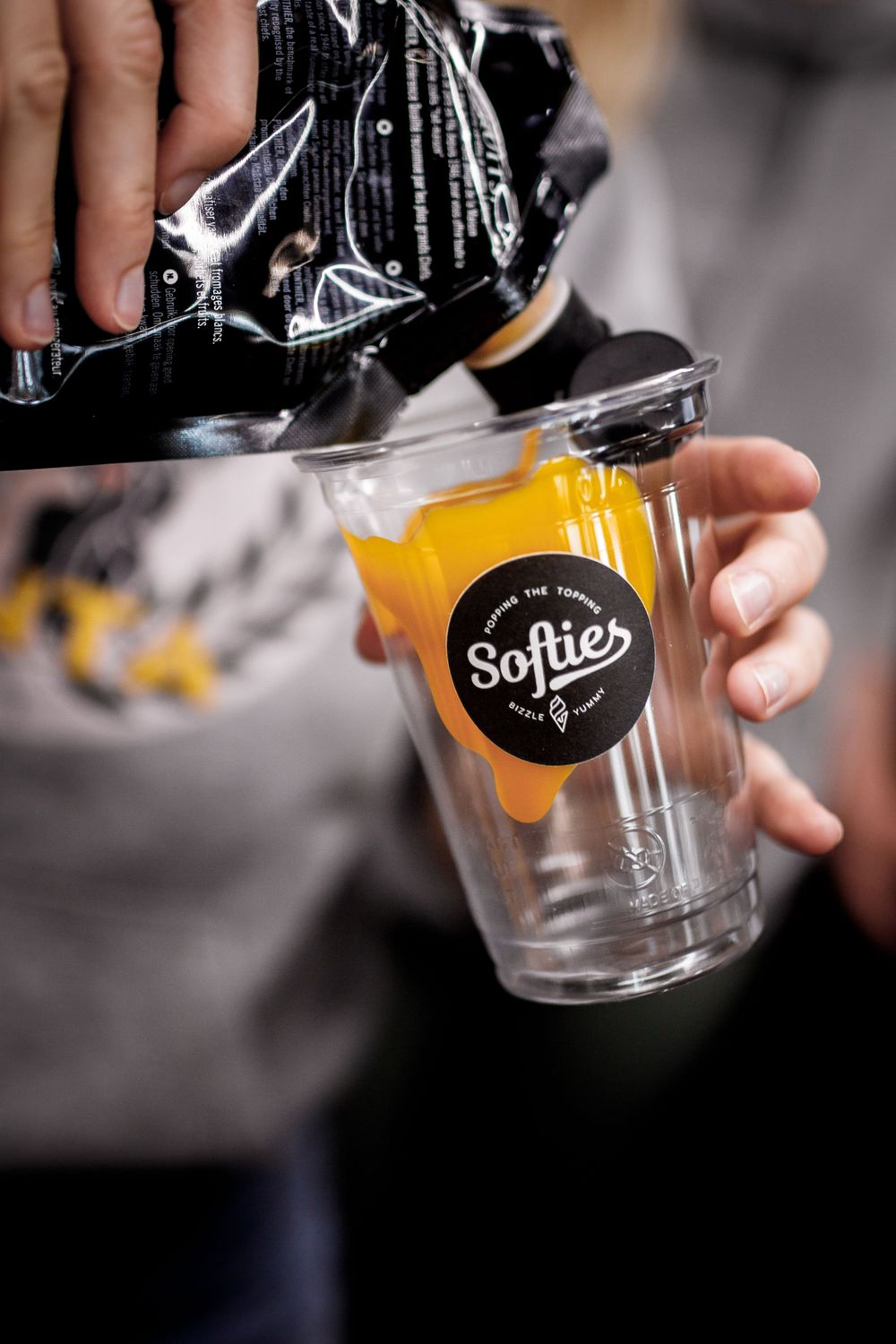 Gelbe Flüssigkeit wird in einen durchsichtigen Softies-Glasbecher mit schwarzem Logo gegossen.