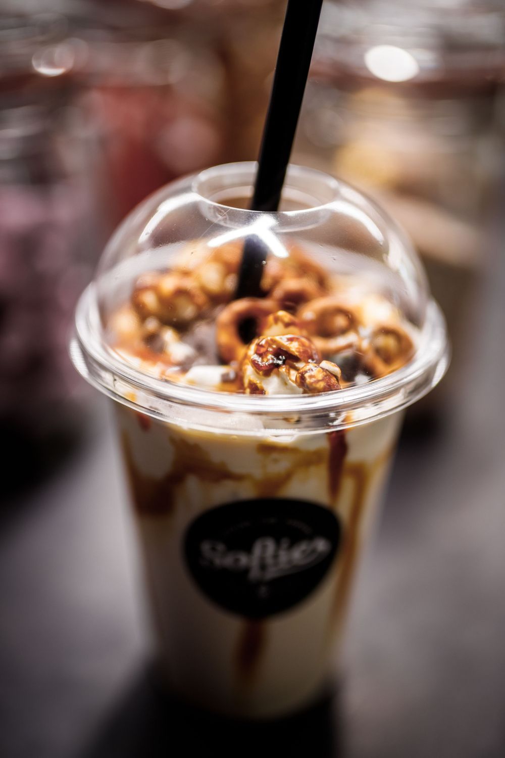 Nahaufnahme eines Eiskaffeegetränks mit Karamellstreuseln und kandierten Nüssen in einem Plastikbecher mit schwarzem Strohhalm.