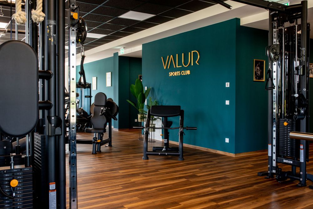 Modernes Fitnessstudio mit blaugrünen Wänden, Holzböden und Trainingsgeräten in der Valur-Trainingsanlage.