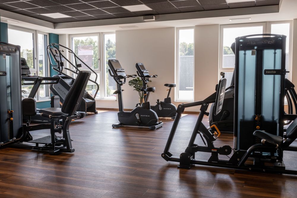 Modernes Fitnessstudio mit Cardiogeräten und Kraftgeräten auf Hartholzboden und natürlichem Licht.