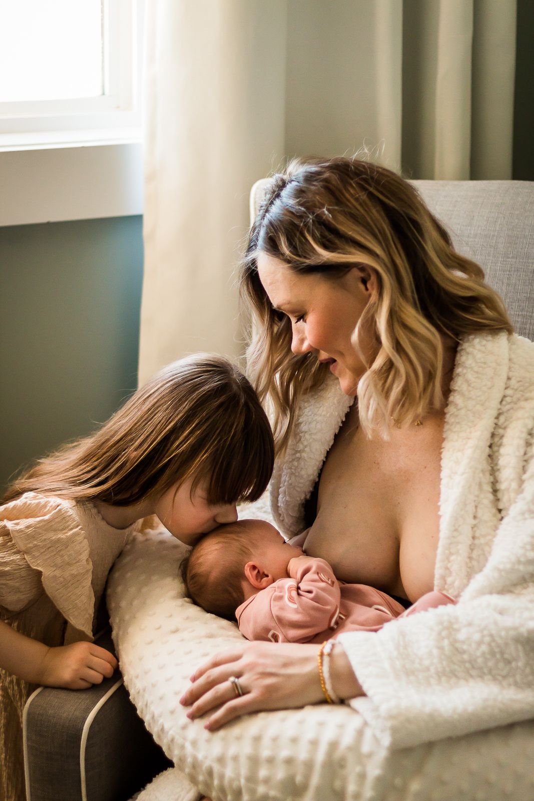 Mom breastfeeding new baby with daughter looking on during lifestyle session at home in Calgary AB