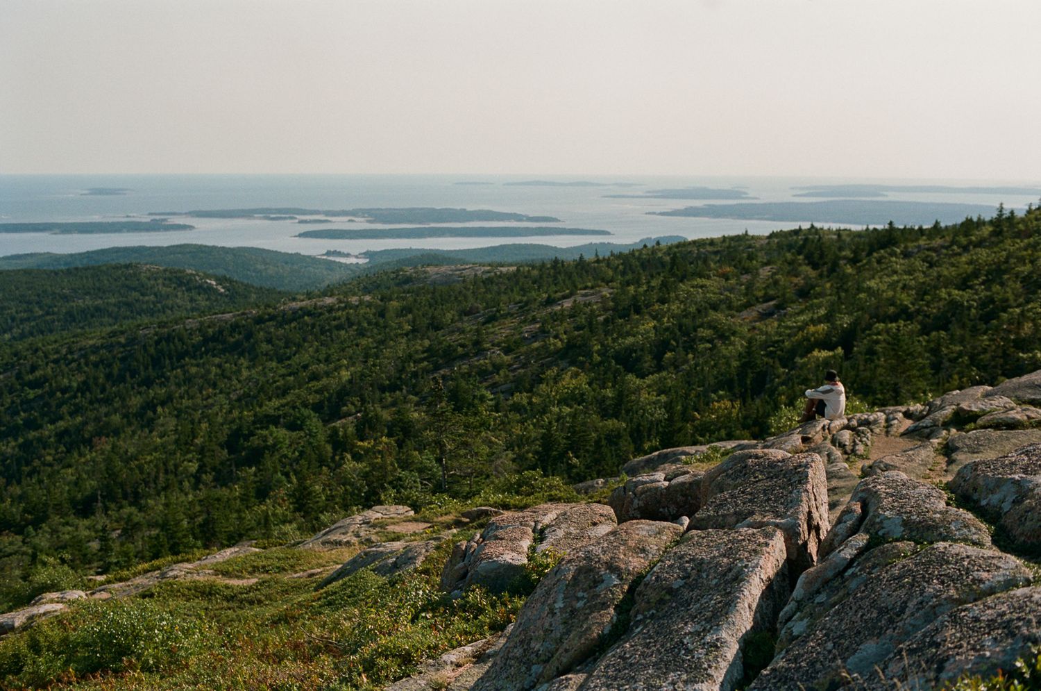 Scenic mountain vista overlooking forested hills and distant lakes from rocky overlook.