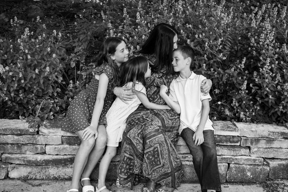 Black and white portrait of family sitting together on stone wall.