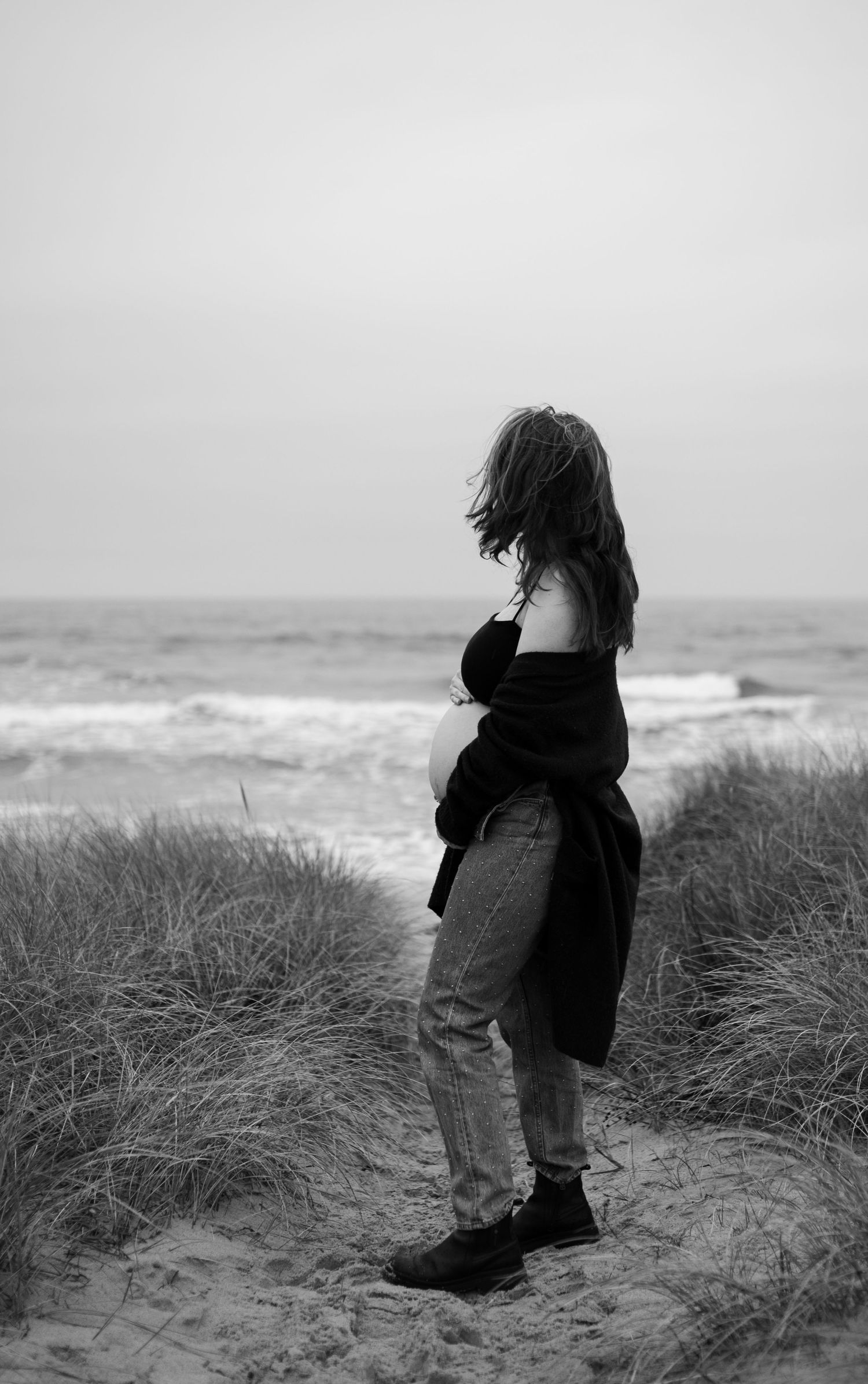 Black and white portrait of someone standing on coastal dunes overlooking the ocean.