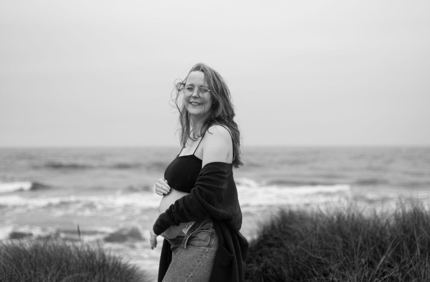 Black and white photo of someone standing on beach dunes with waves crashing in the background.