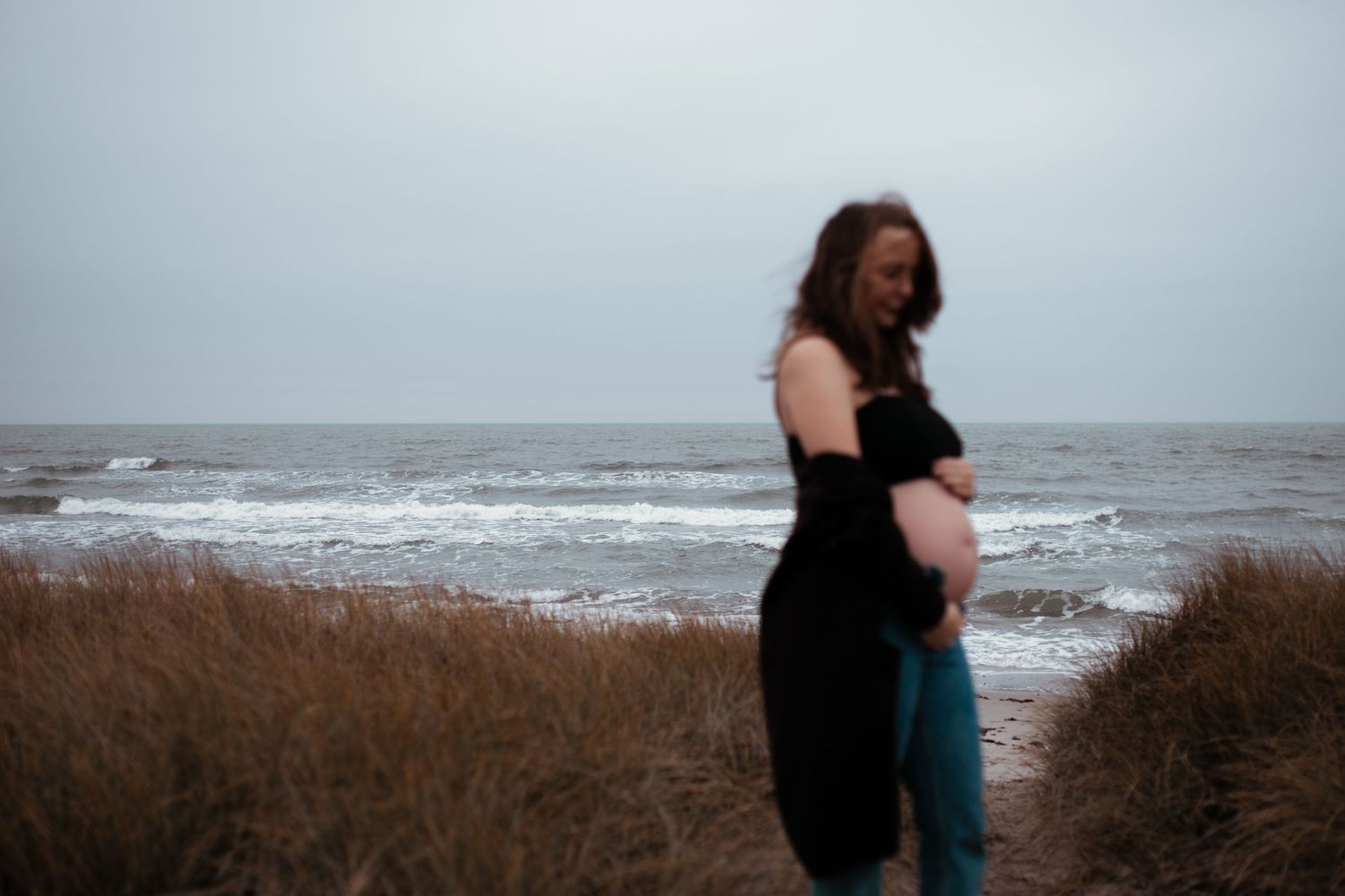 A side view of someone standing among beach grass with ocean waves in the background.