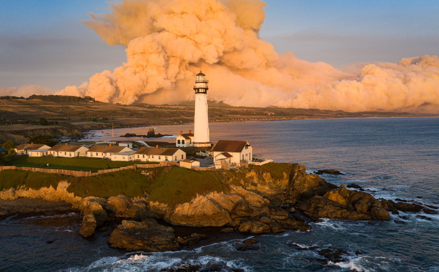 Pigeon Point Lighthouse on rocky California coast at sunset with dramatic orange clouds overhead.