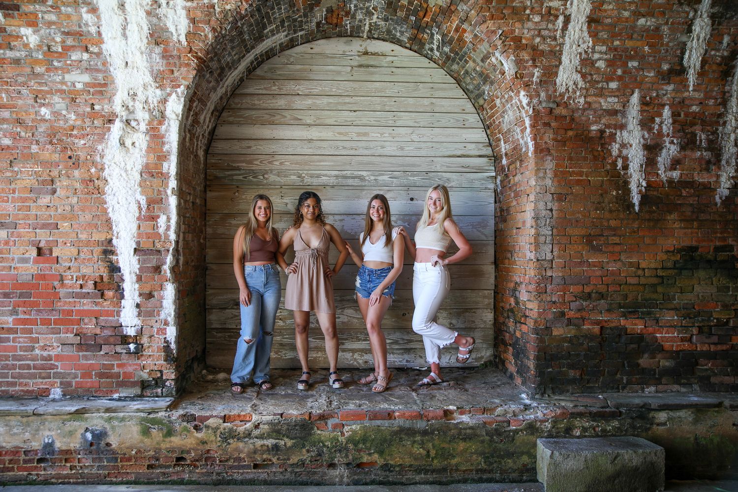 Group poses under brick archway in casual summer outfits.