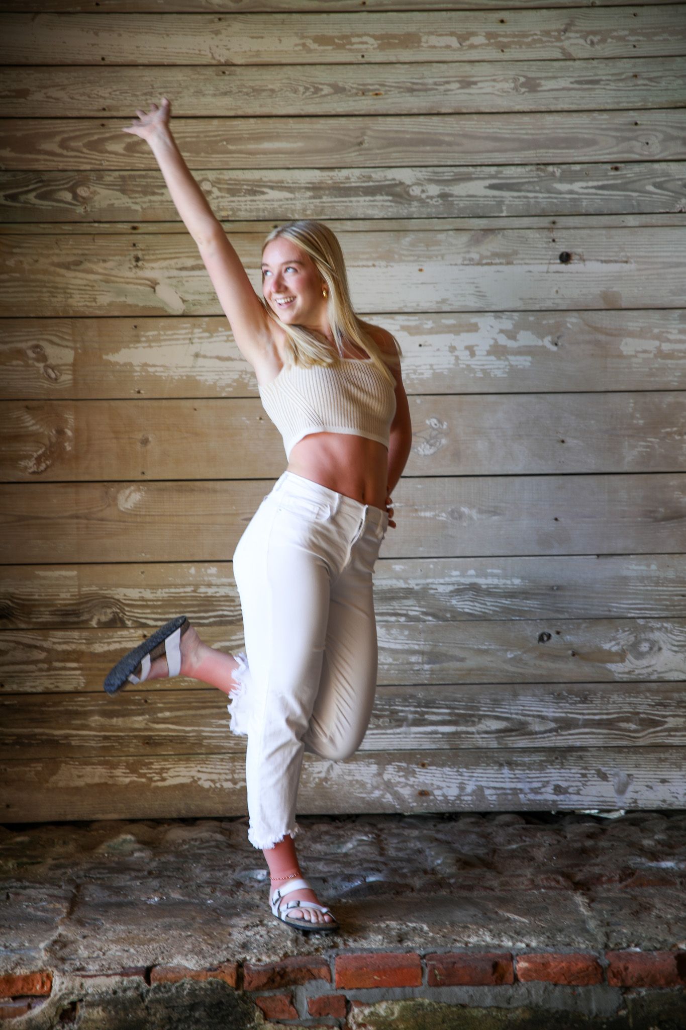 Energetic pose in white outfit against rustic wooden wall background.