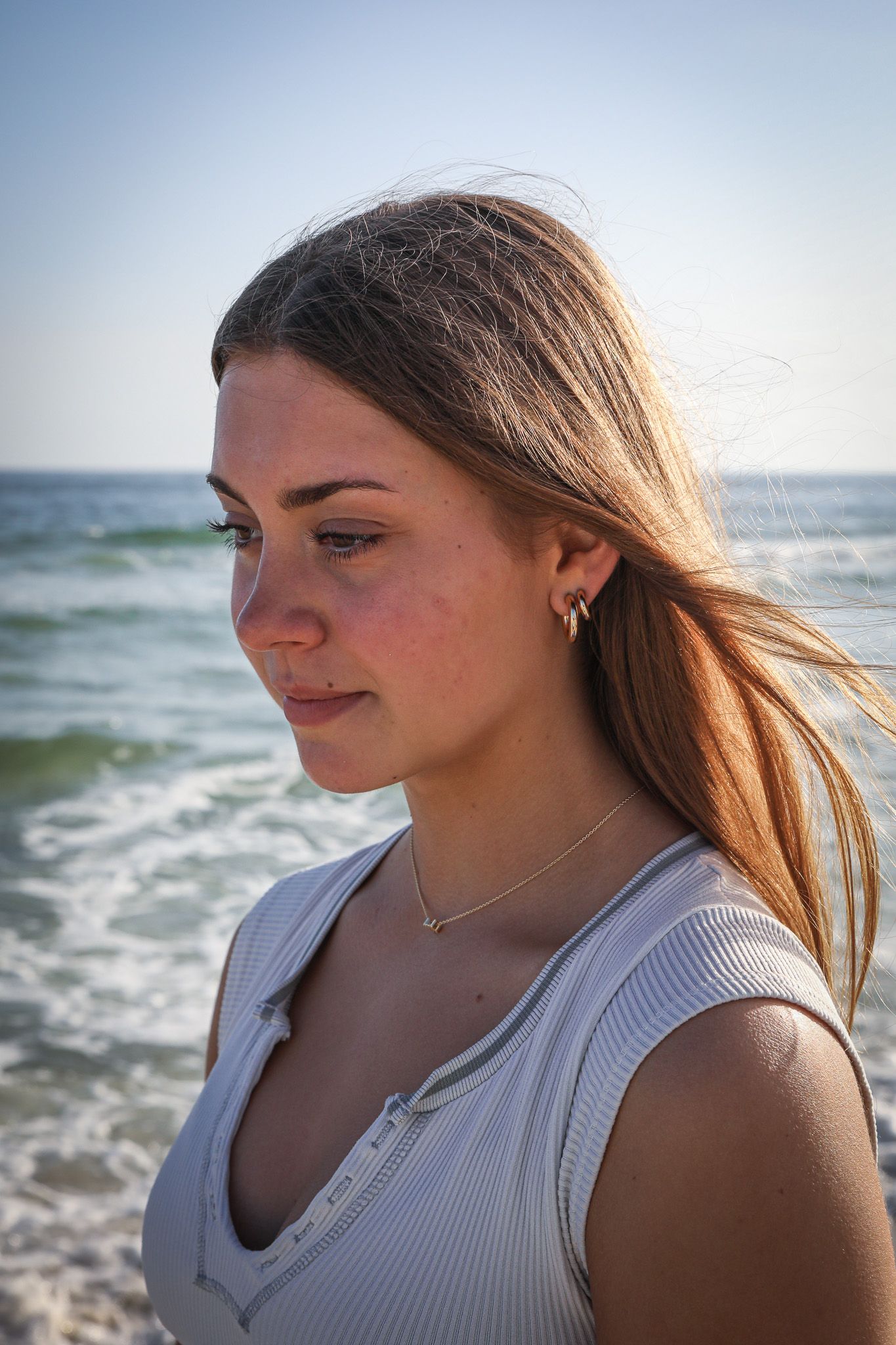 Portrait of a woman with windswept hair gazing thoughtfully at the ocean.