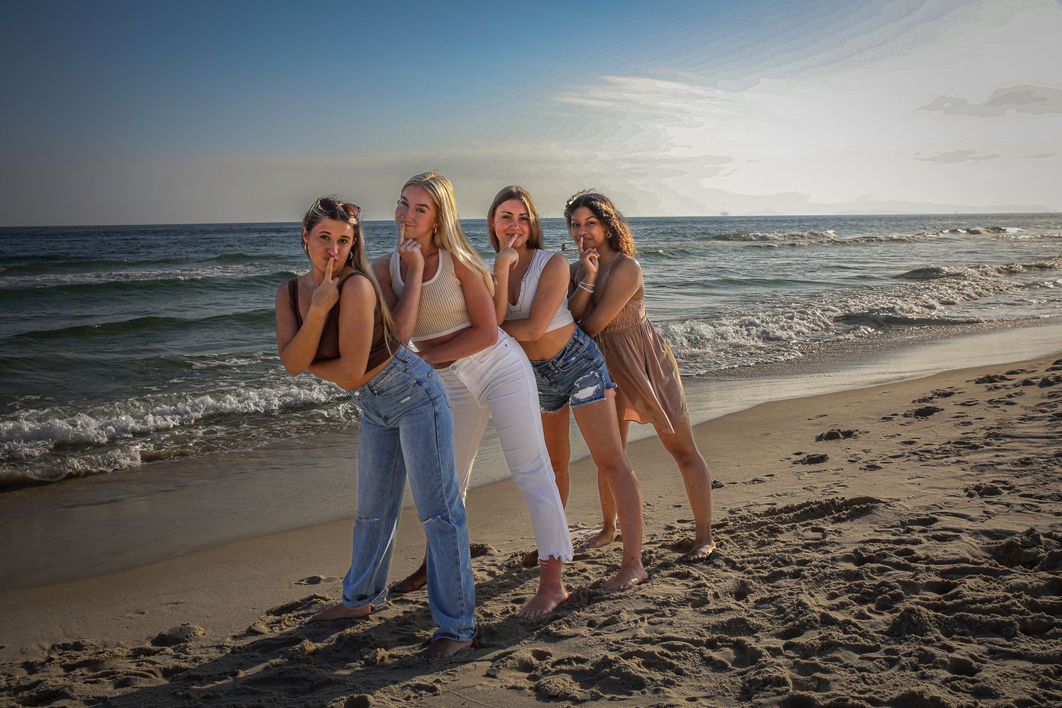 Group of friends posing together on sandy beach at sunset.