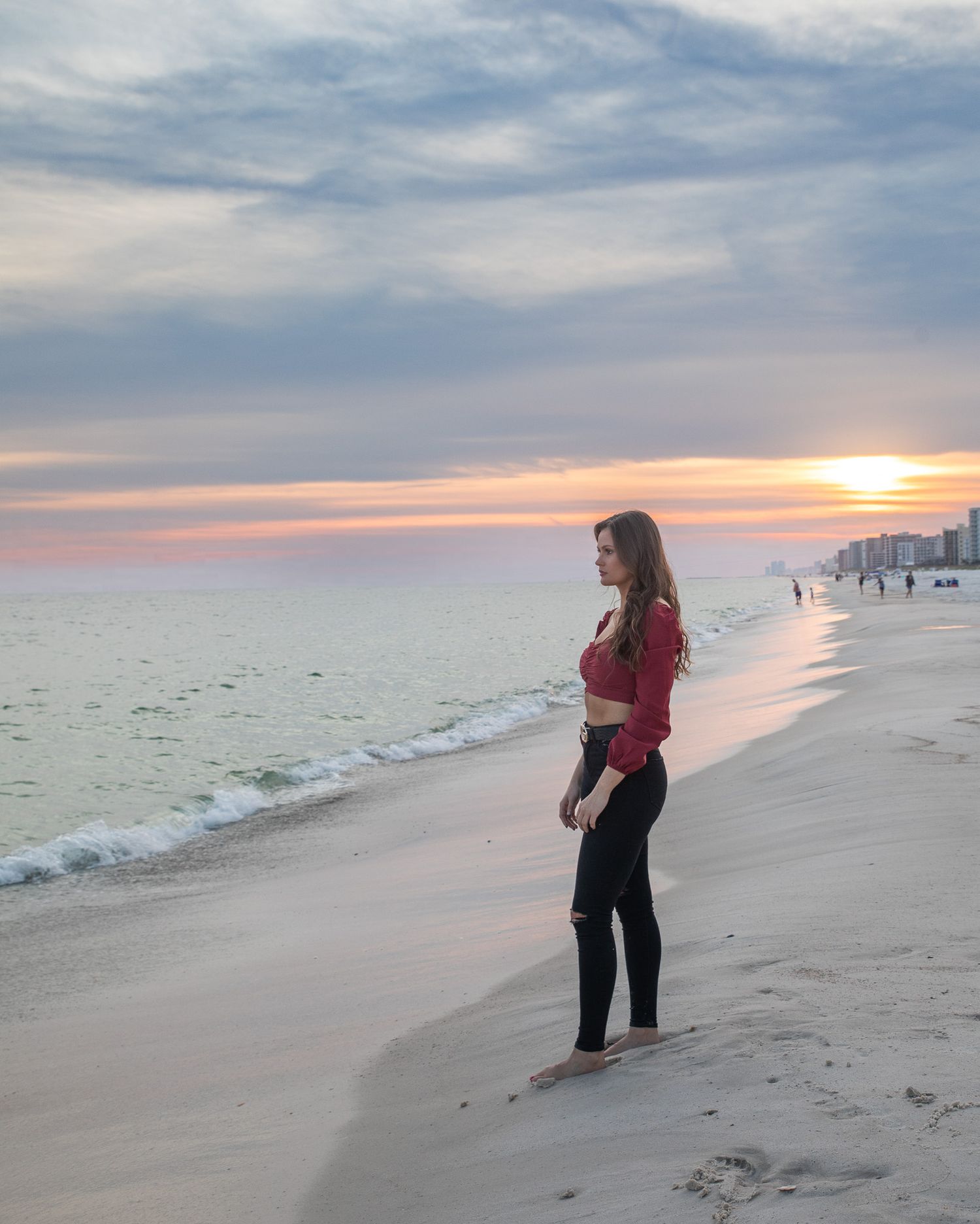 Person in red top standing on beach watching sunset over ocean.