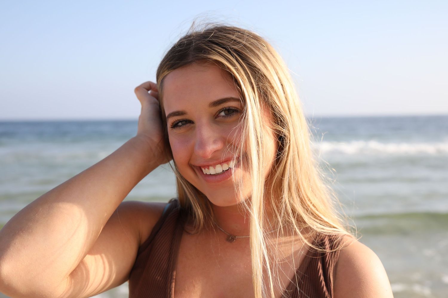 Portrait of beachgoer with flowing hair smiling by the ocean on a sunny day.