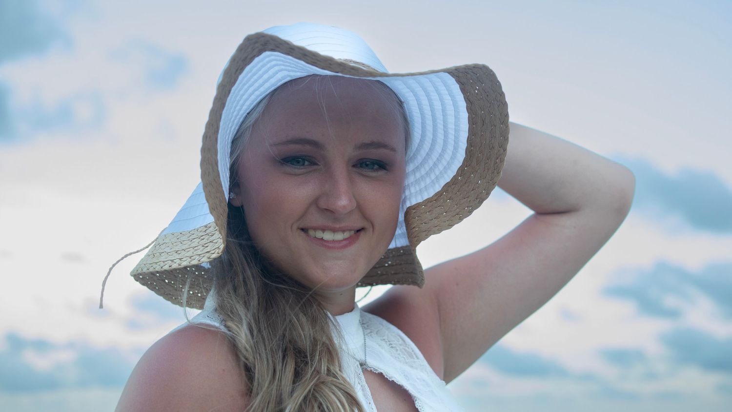 Portrait of someone wearing a white floppy sun hat on a sunny day.