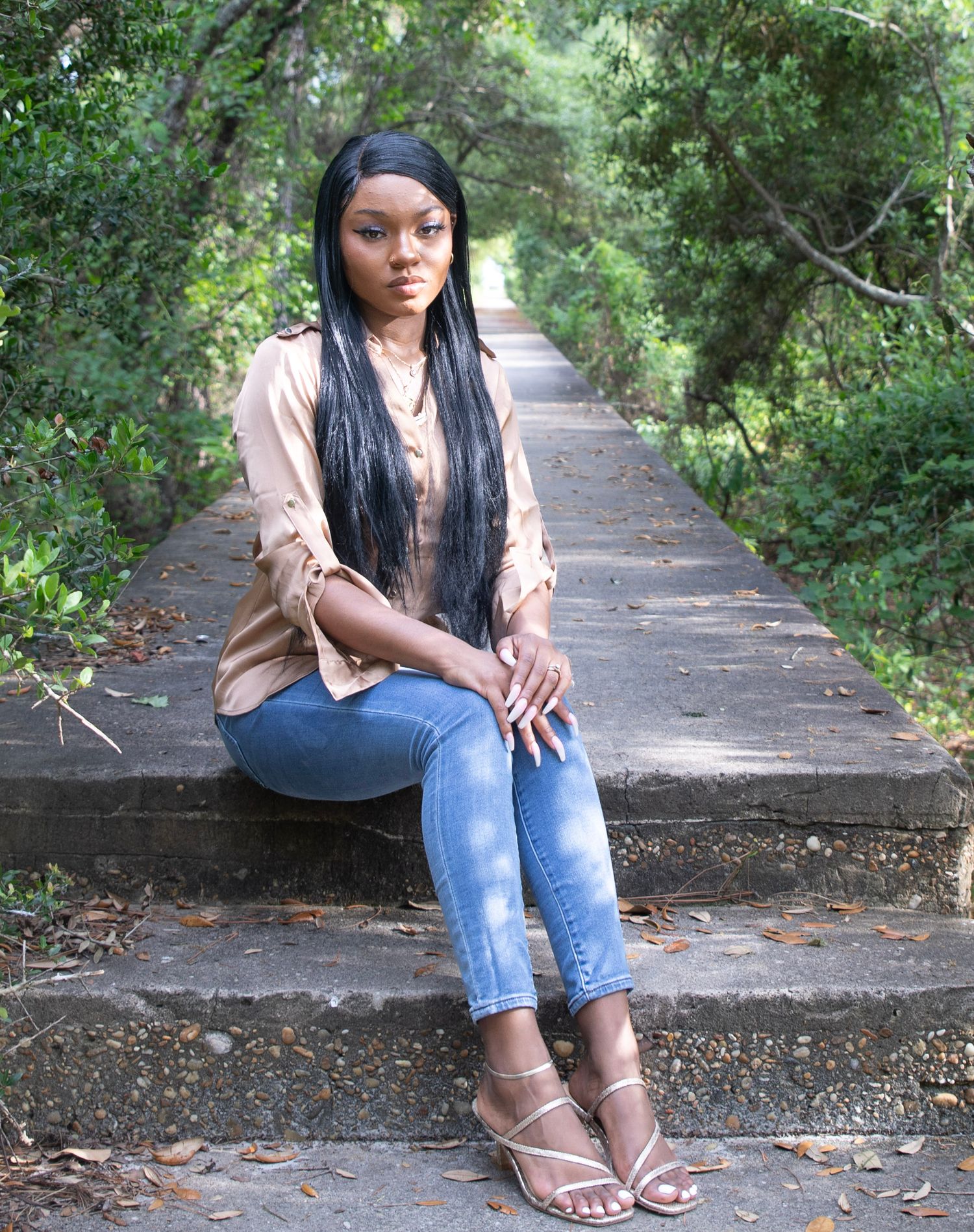 Casual portrait on wooded path with someone wearing beige top and distressed jeans.