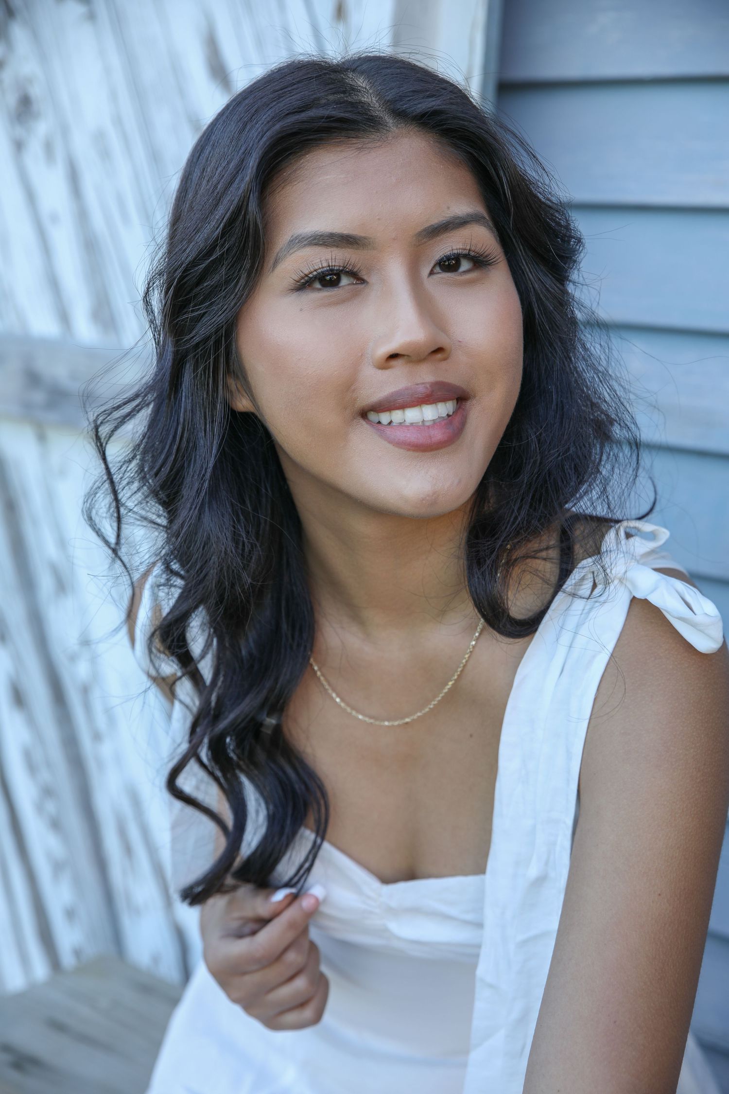 Portrait against white wooden wall wearing delicate white top and dainty necklace.