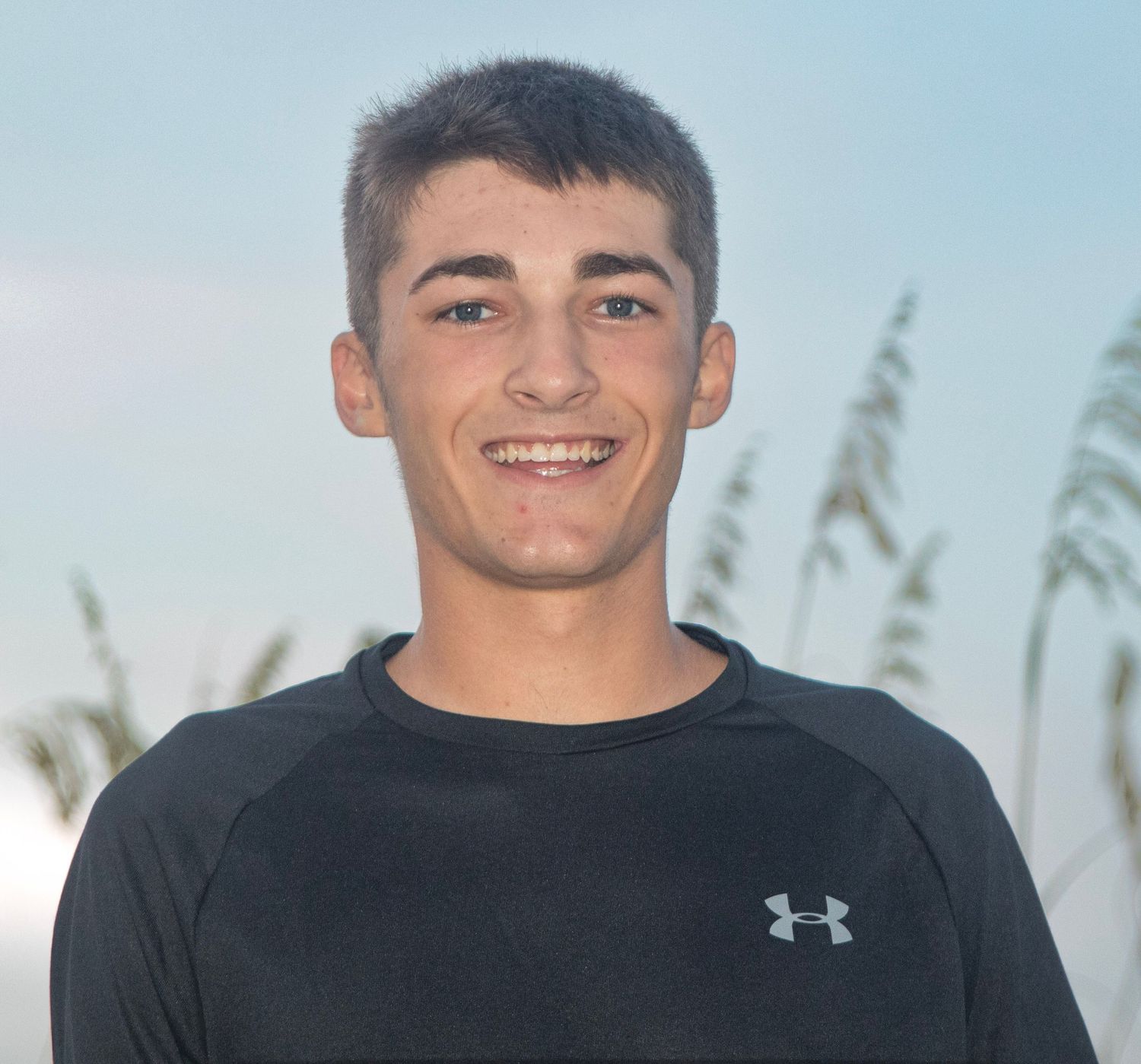 Person wearing black Under Armour shirt against coastal background with sea oats.