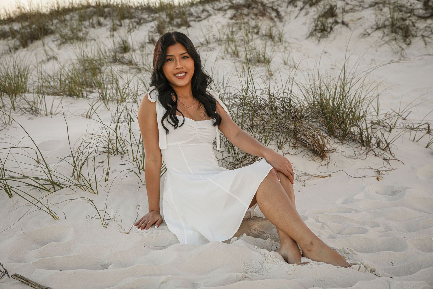 Person in white sundress poses gracefully on sandy beach dunes.