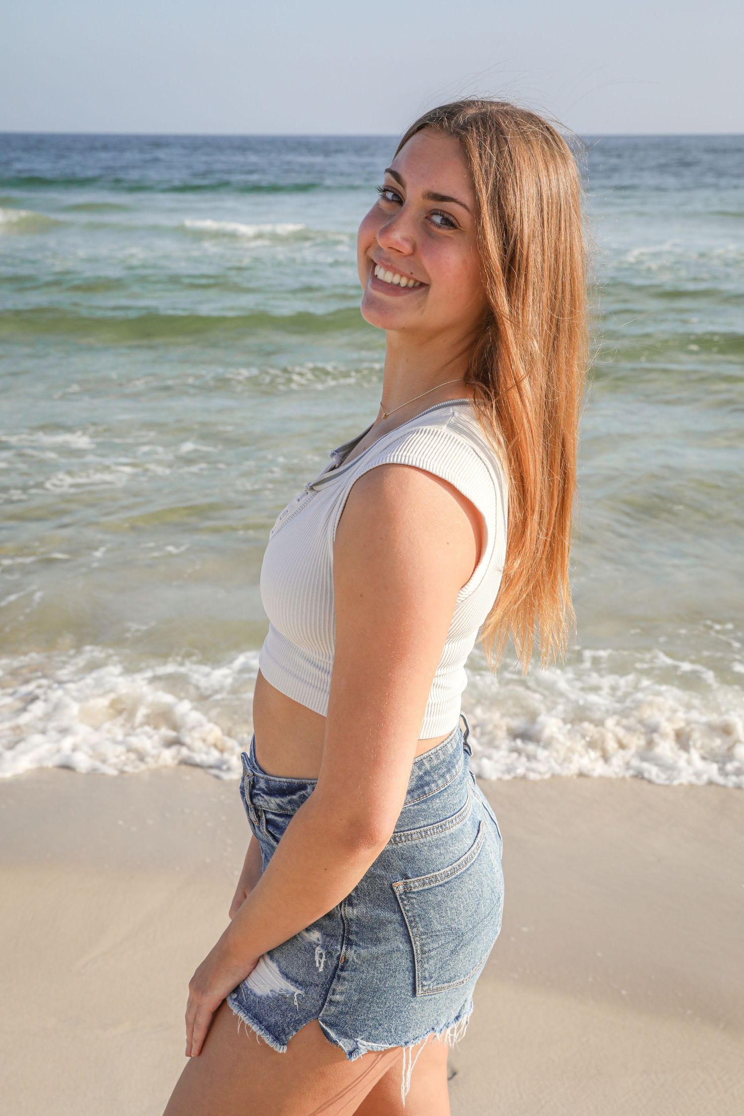Casual summer portrait of person in white top and denim shorts on sandy beach.