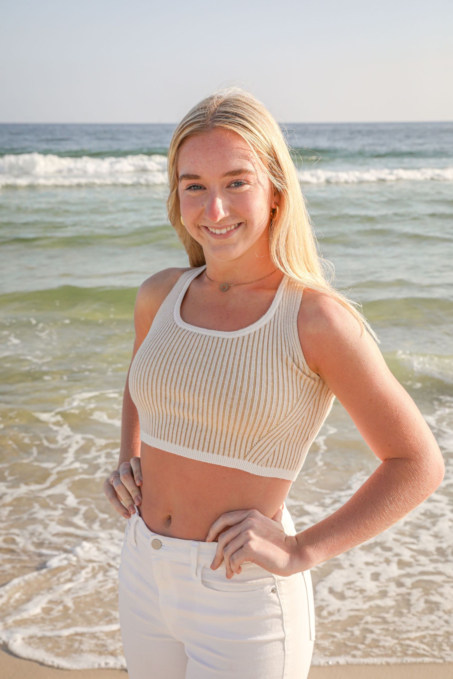 Beach portrait of person in white crop top and pants posing by ocean waves.