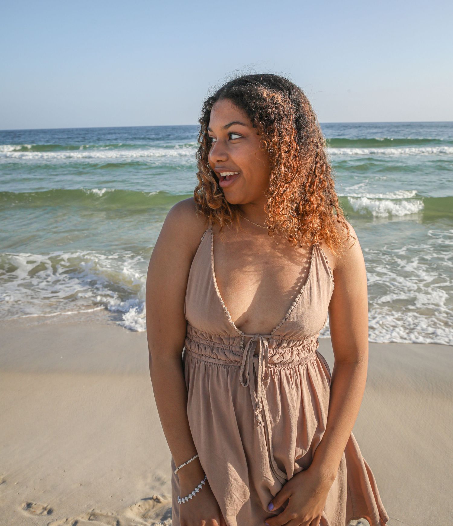 Joyful beachgoer in tan dress smiling against ocean backdrop.