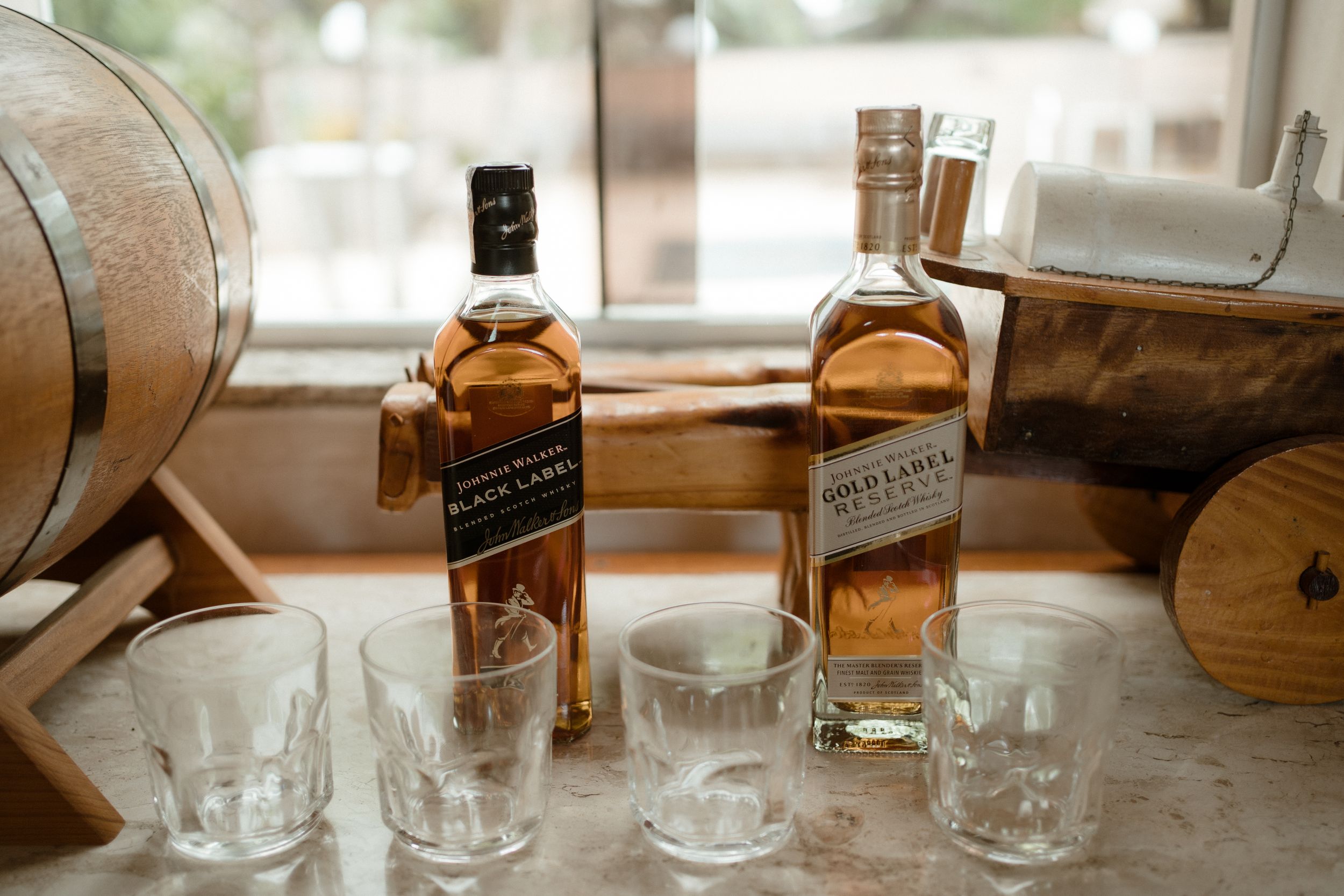 Bottles of Johnnie Walker whiskey with glasses displayed near wooden barrels.
