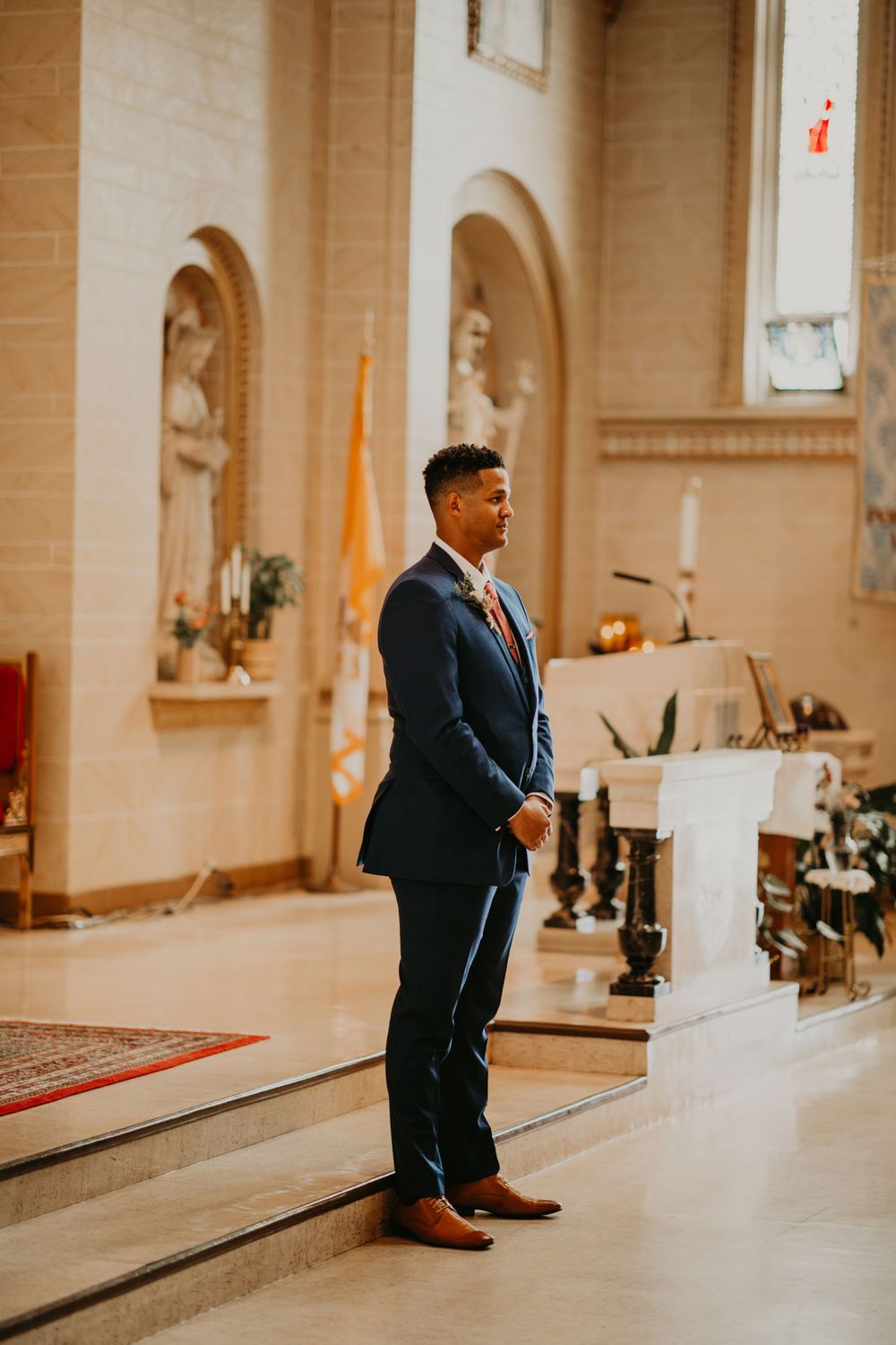 Groom in navy suit stands at church altar awaiting his bride during wedding ceremony.