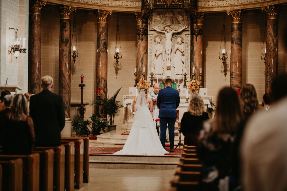 Bride and groom stand at ornate church altar before crucifix during traditional wedding ceremony.