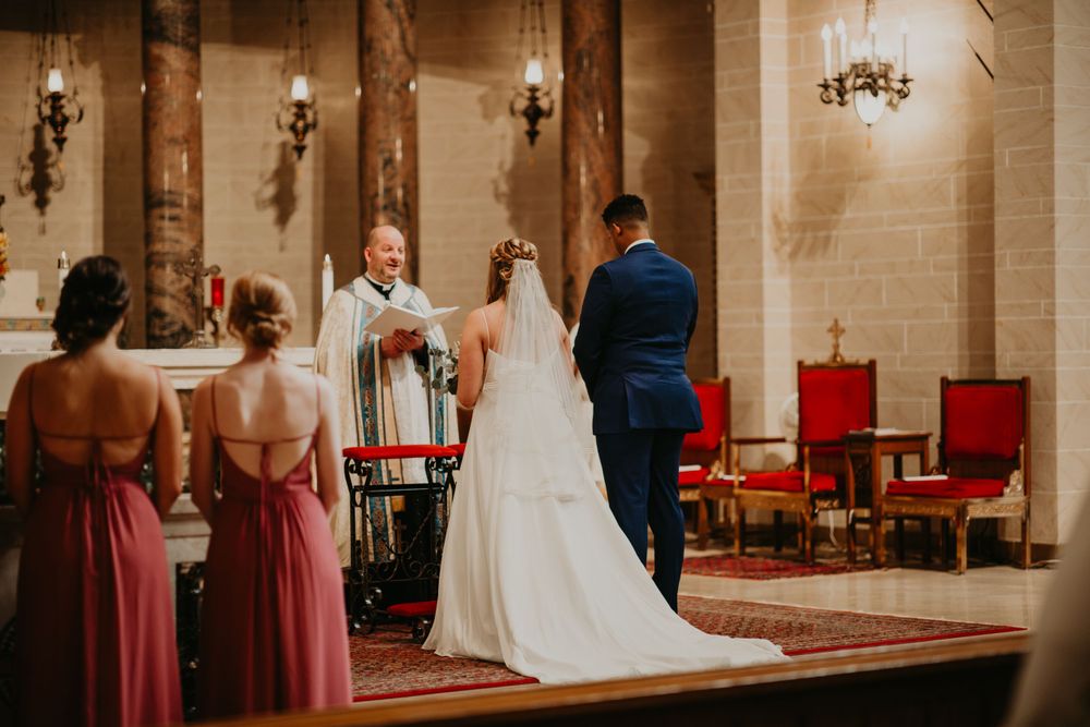 Bride and groom stand at altar with bridesmaids in pink dresses during elegant church wedding.