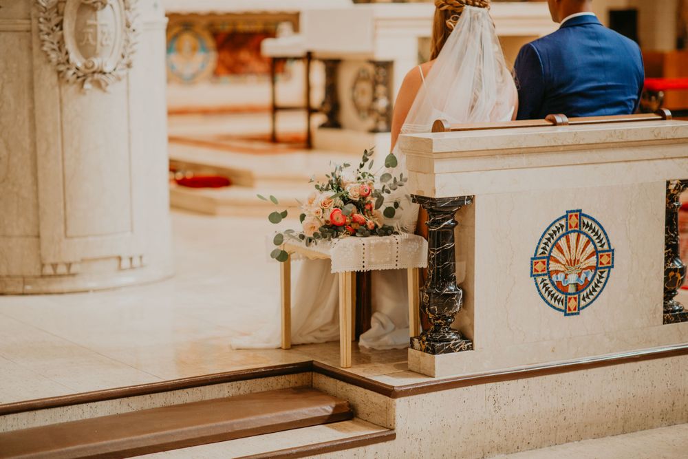 Close-up of floral wedding arrangement resting on ornate church pew during ceremony.