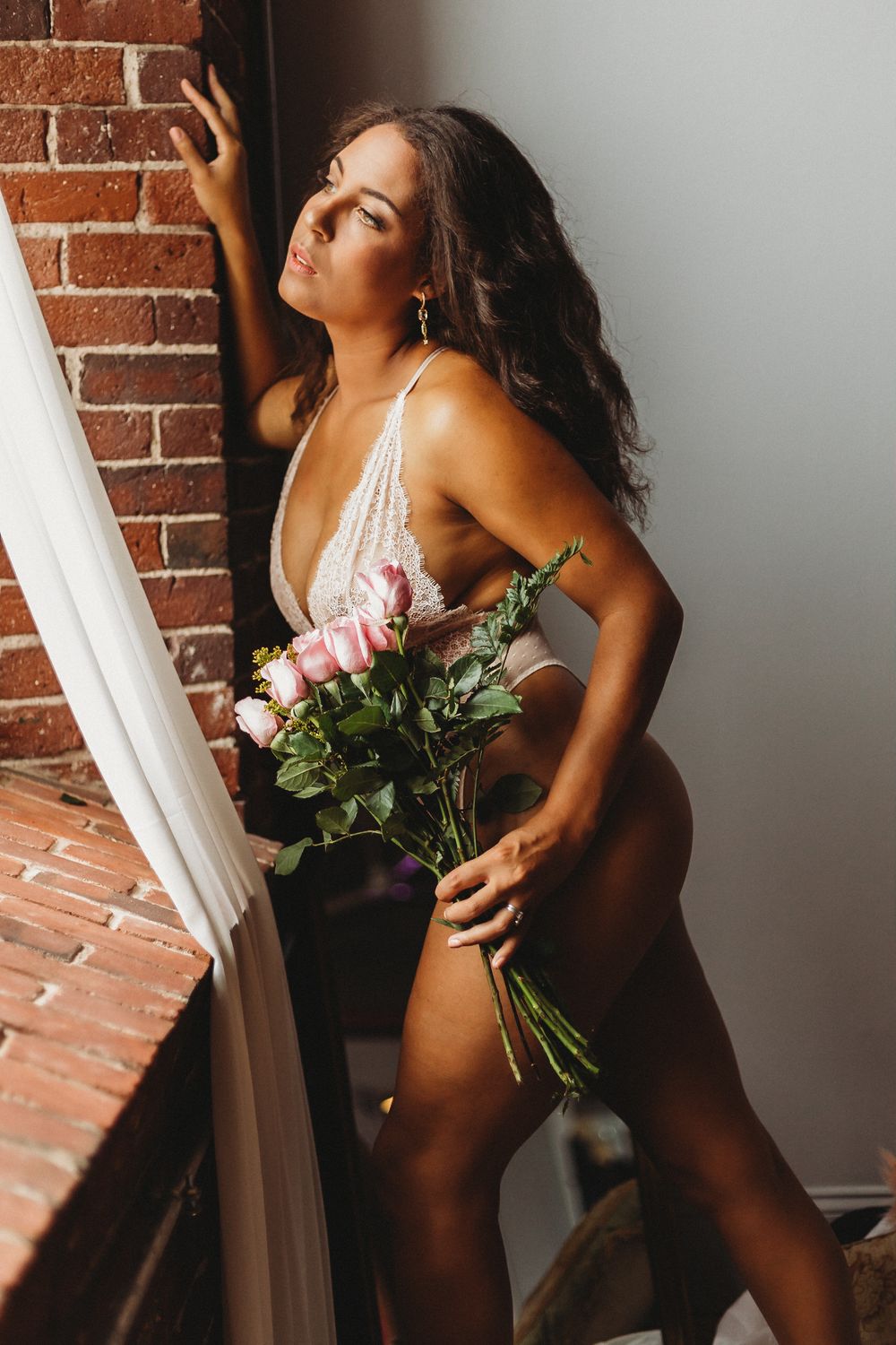 Romantic portrait holding fresh flowers against exposed brick wall with natural lighting.