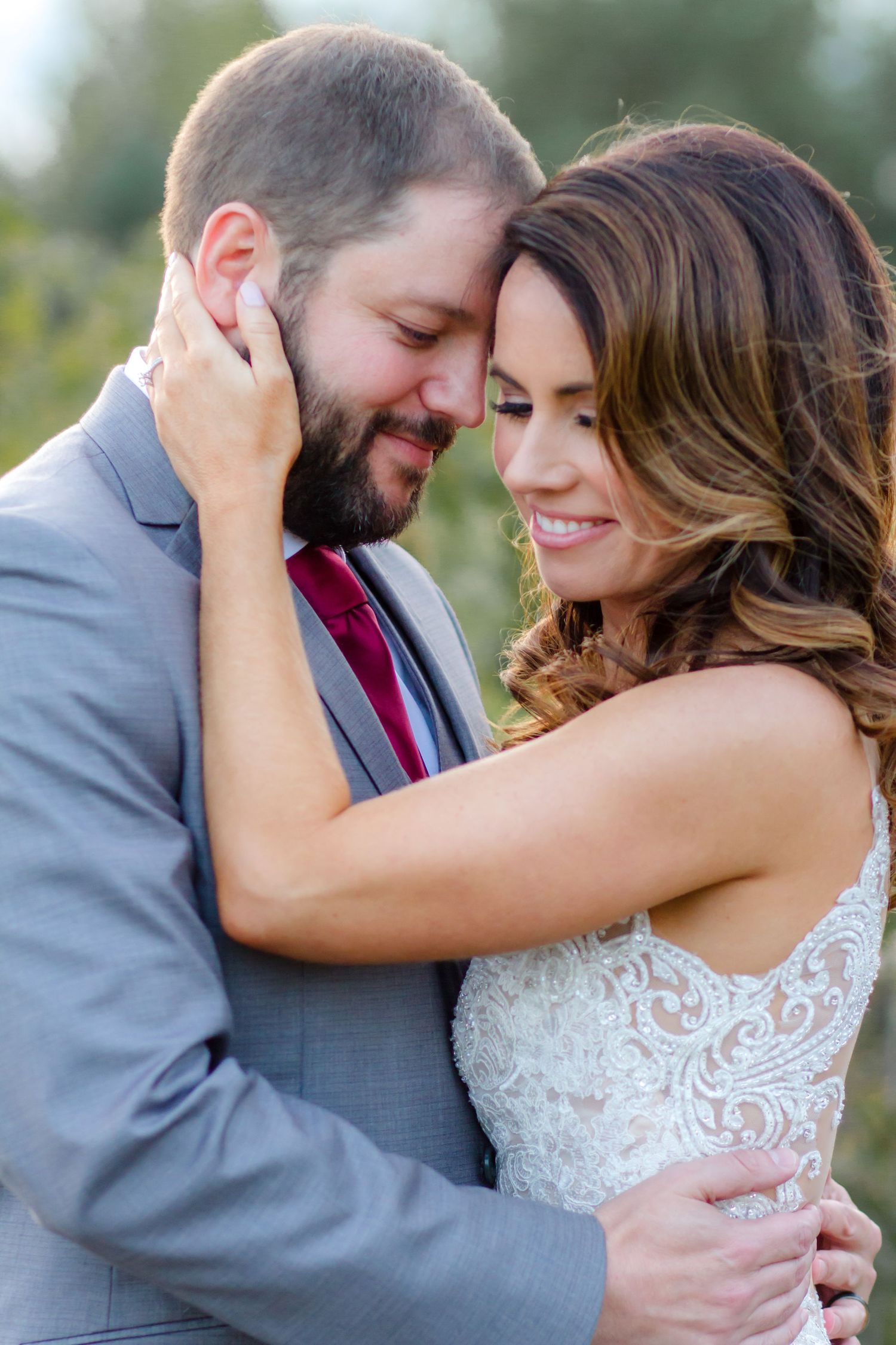 The bridge holding the grooms face in her hand and embracing him looking down and smiling.
