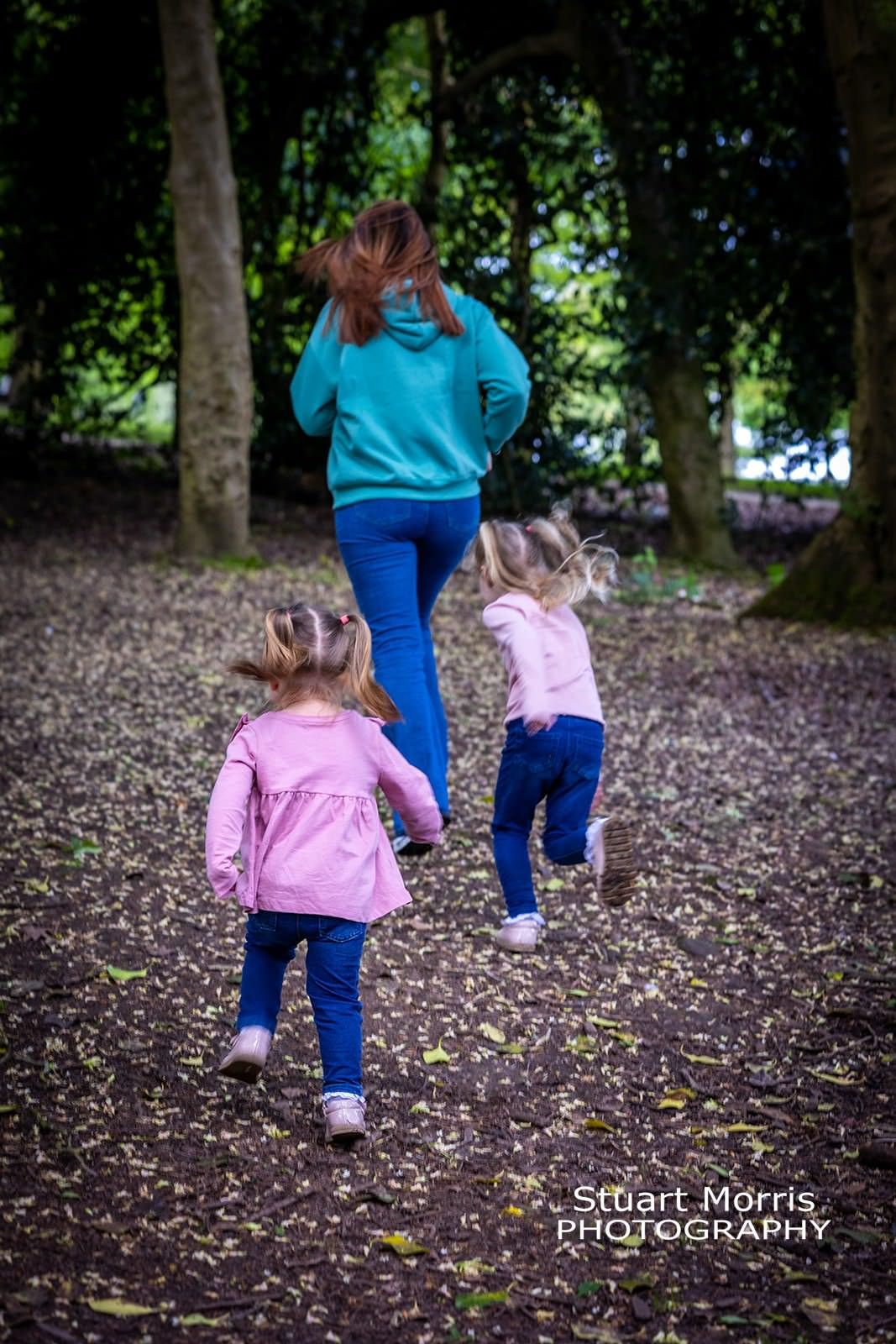 mum chased by her 2 little girls in woodland at Walton hall park. relaxed outdoor portrait session.