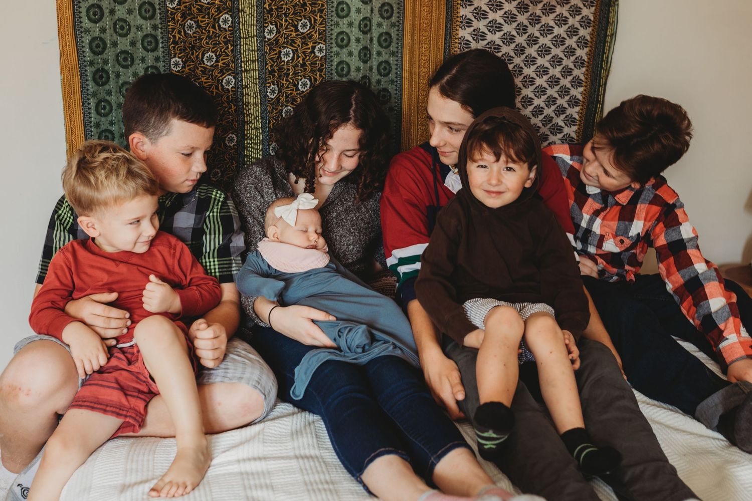 Group of brothers and sisters holding baby on a bed