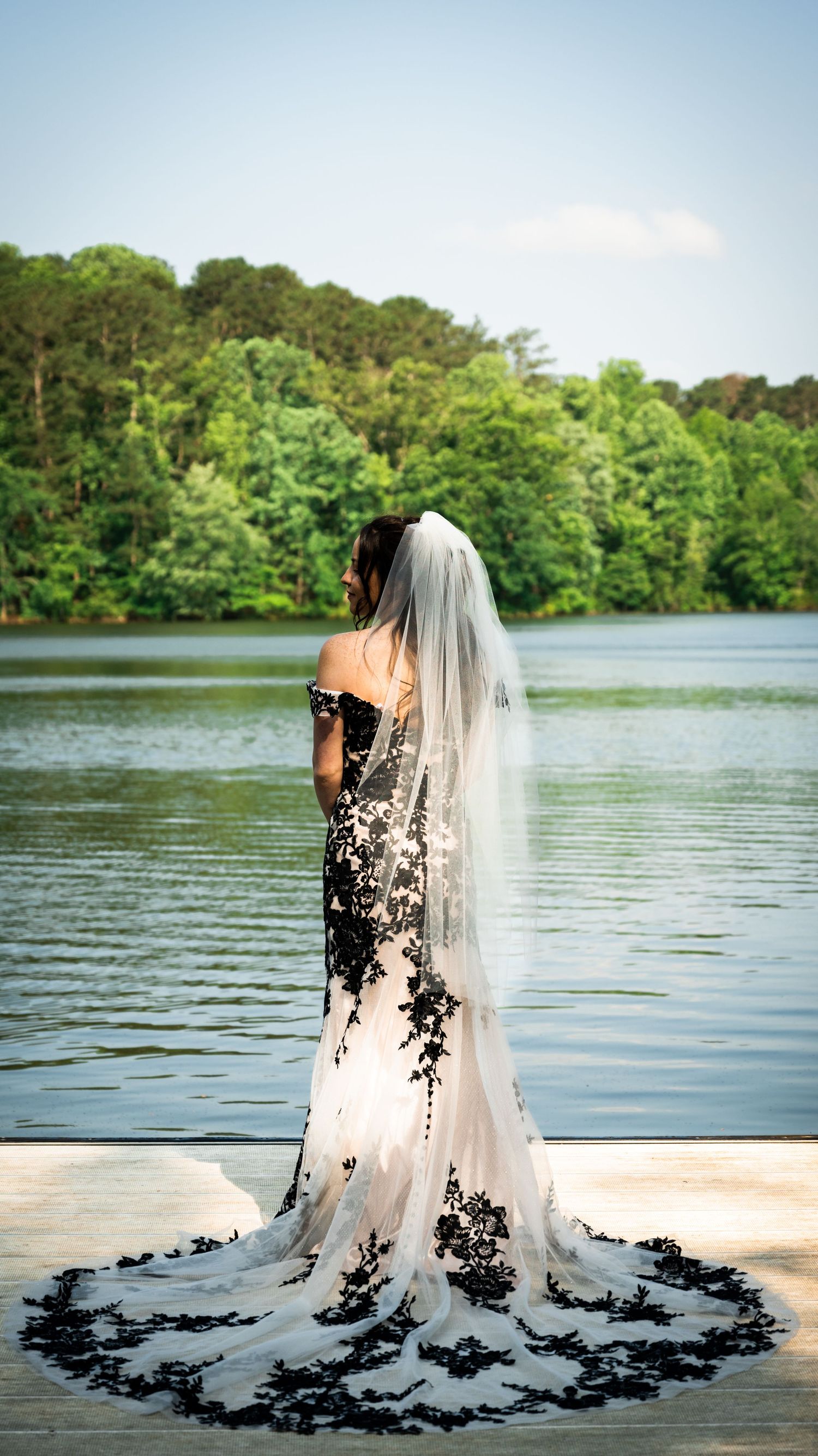 An elegant white wedding gown with black lace appliques photographed by a serene lake.