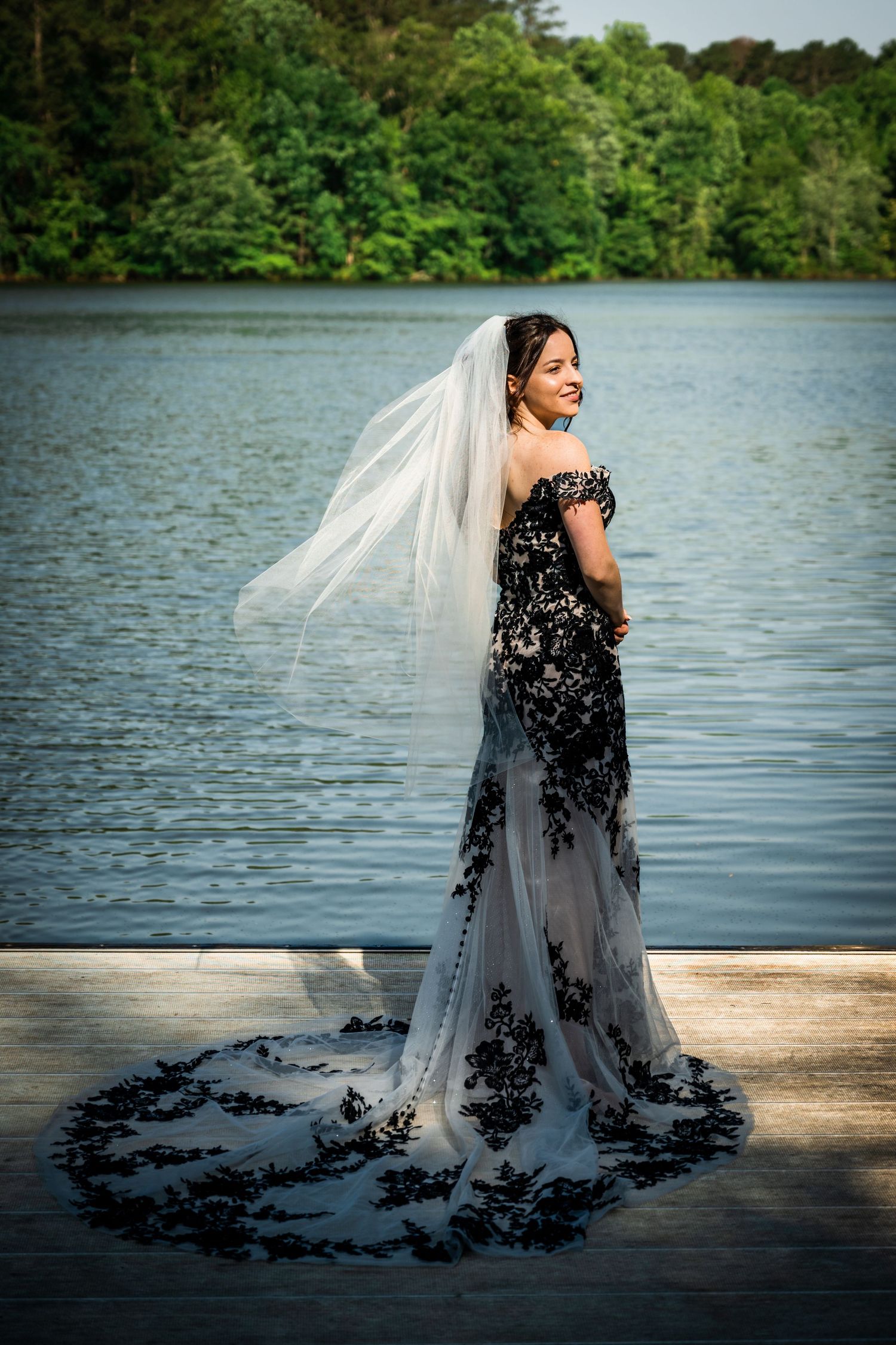 A stunning black and white wedding dress with lace details flows across a waterfront deck.