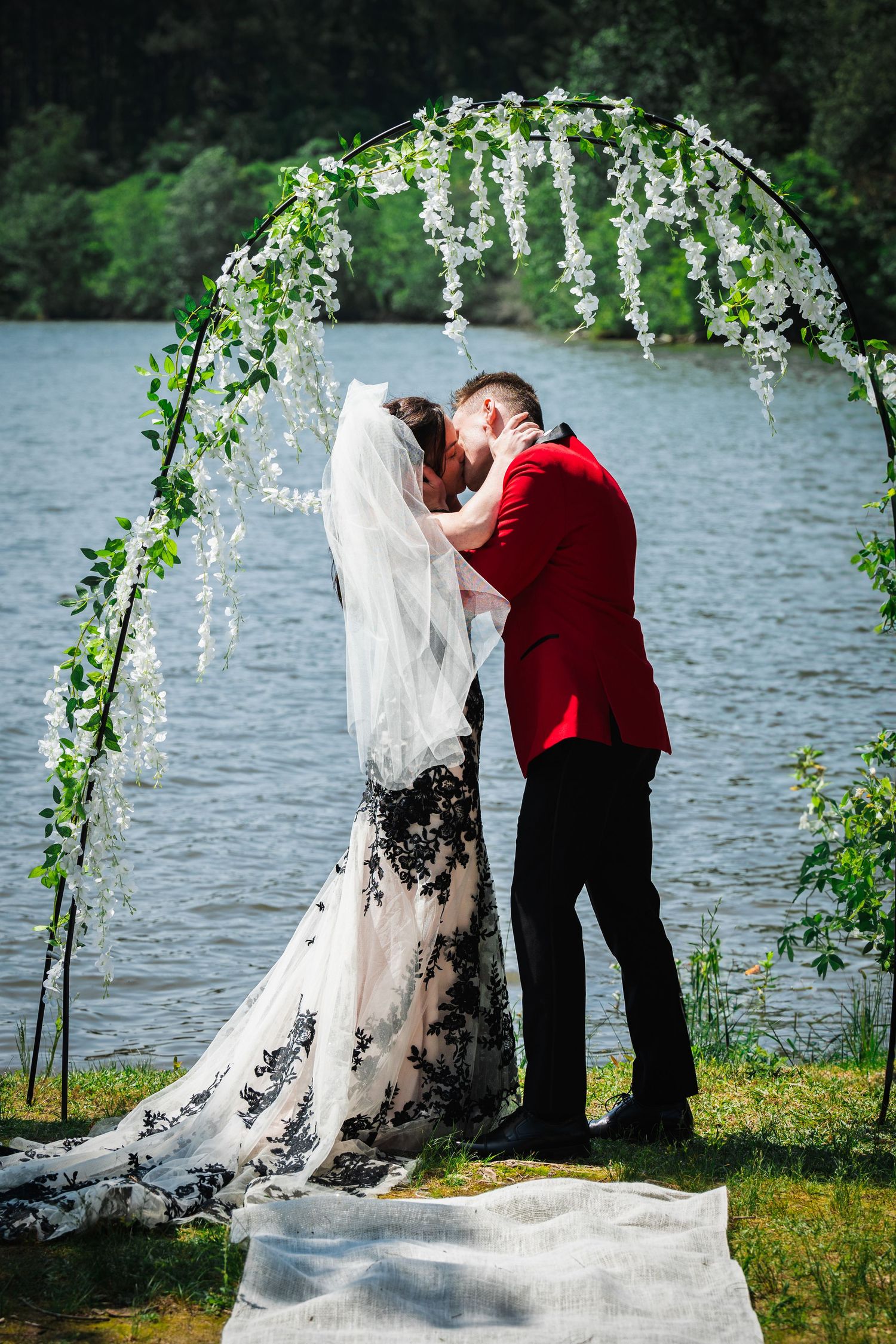 A romantic wedding moment captured under a floral arch by the water.