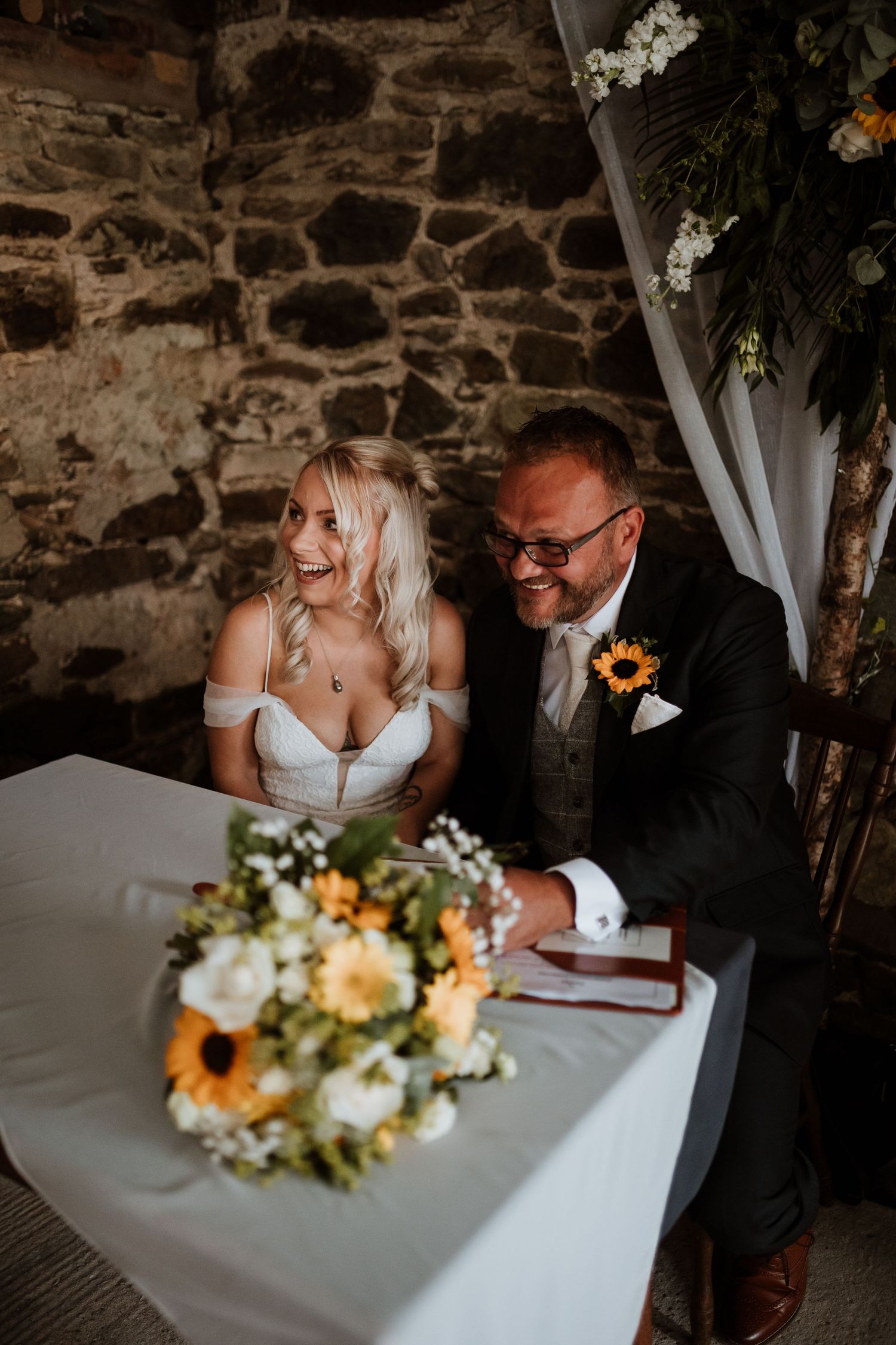 Couple laughing whilst signing the register at Glyngynwydd Wedding Barns, Llanidloes