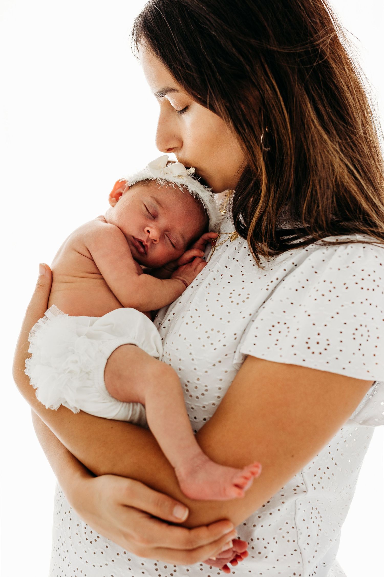 An intimate portrait shows a gentle embrace between parent and newborn against a white background.