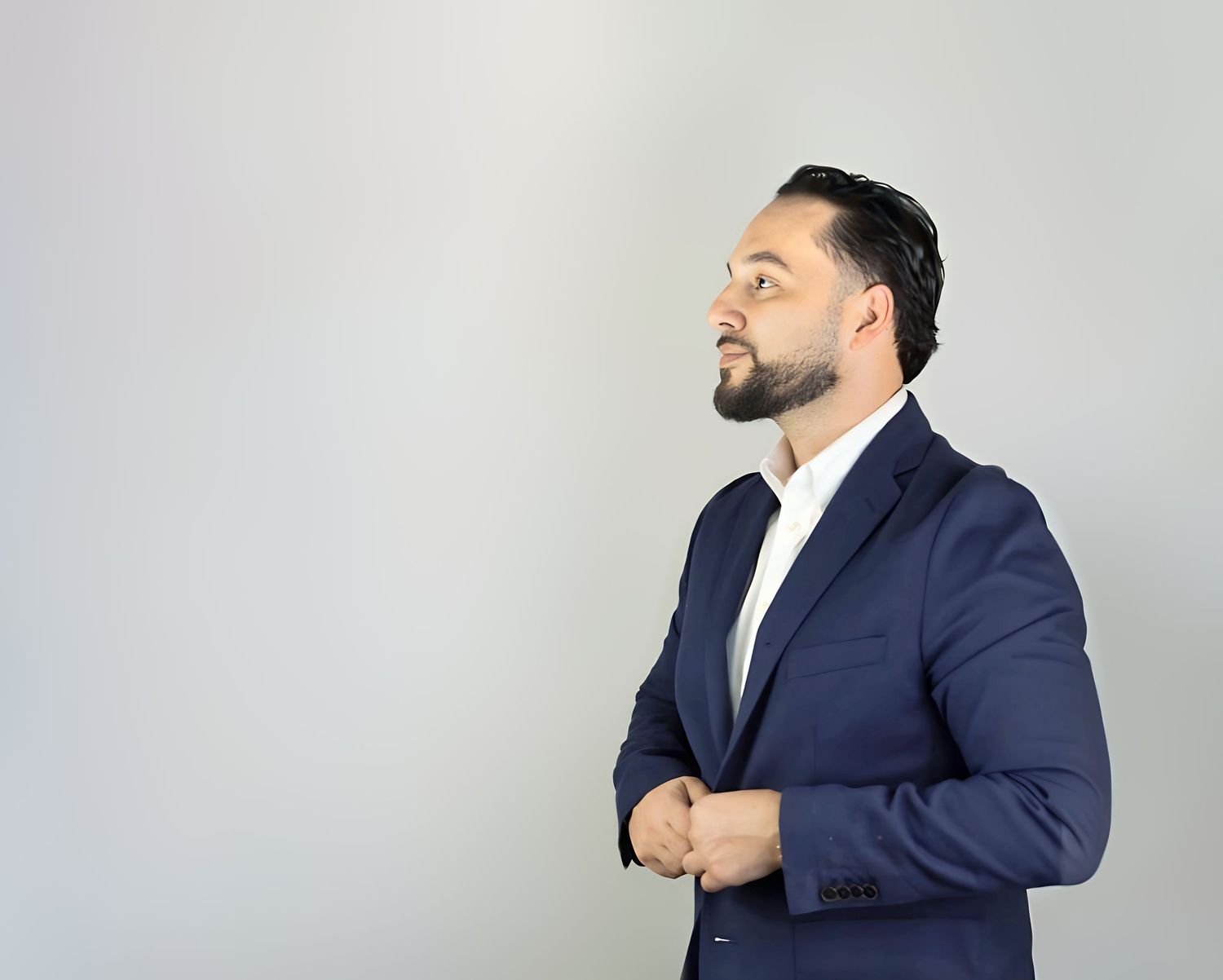 Professional portrait of a person in a navy suit jacket looking thoughtfully to the side against a gray background.