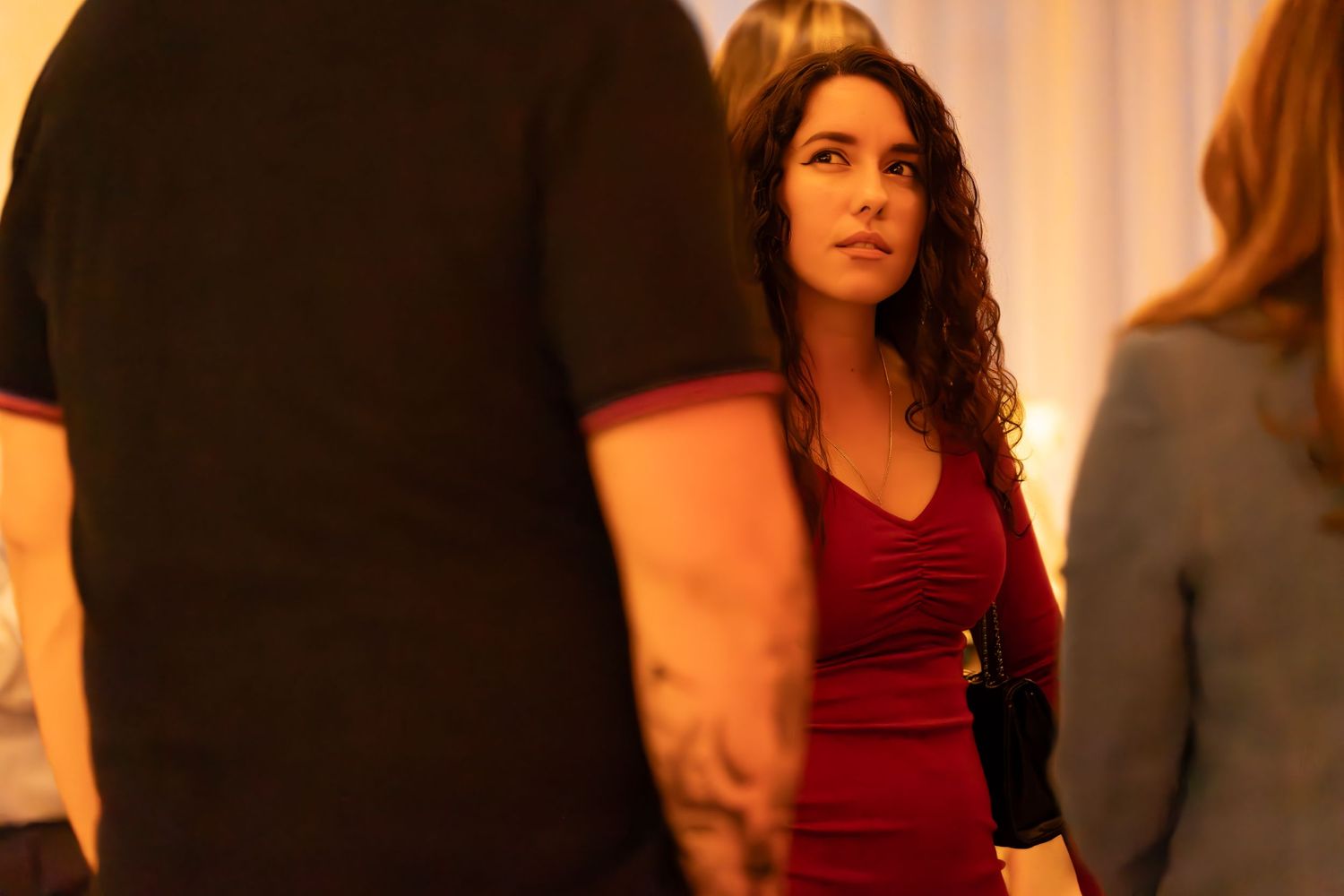 Someone wearing a burgundy dress stands among others in a warmly lit indoor setting.