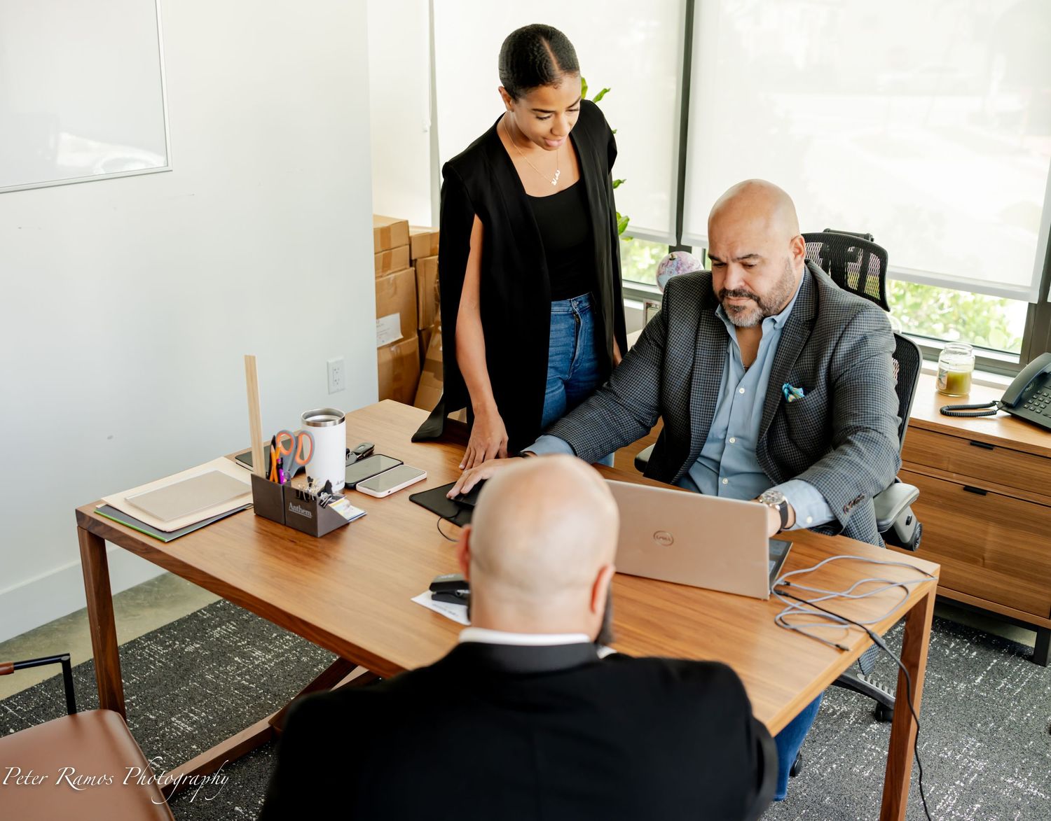 Business professionals meet at wooden desk in bright office space during daytime meeting.