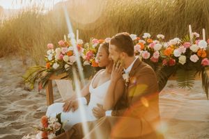 Golden hour sunlight illuminates a beachside wedding ceremony with floral arrangements.