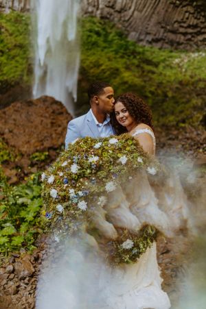 Wedding portrait with couple embracing near misty waterfall with floral details.