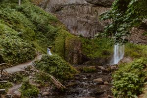 Scenic waterfall cascading down rocky cliffs with lush greenery and hiking path.