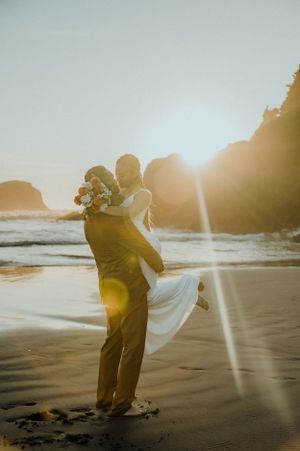 A couple embracing on a sandy beach during golden hour with sunflares.