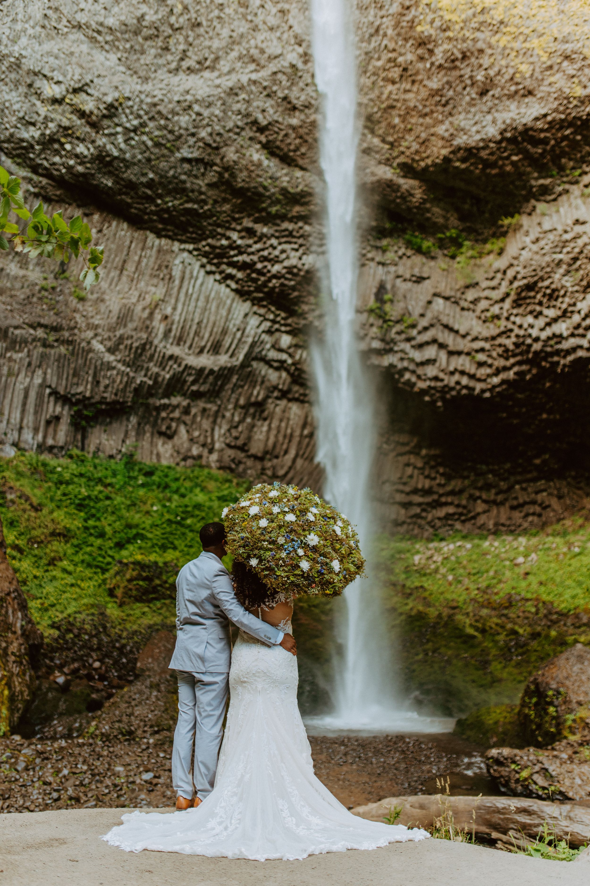 A couple in wedding attire embracing in front of a majestic waterfall.