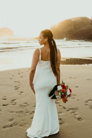 A white wedding dress and red bouquet against the backdrop of a sunset beach.