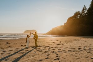 Silhouettes walking along a scenic beach at sunset with cliffs in the background.