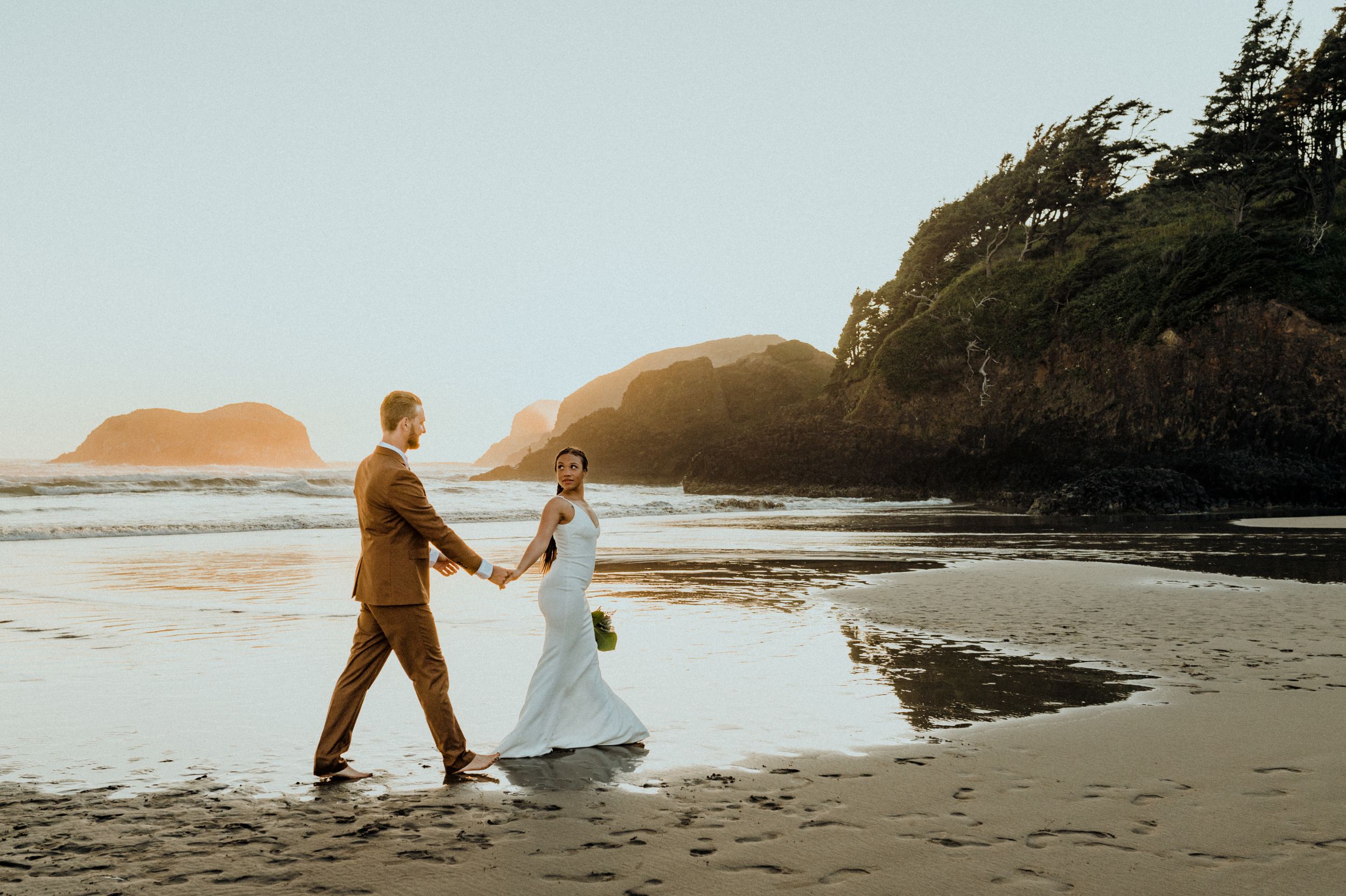 A couple walking hand in hand on a scenic beach with cliffs and ocean views.